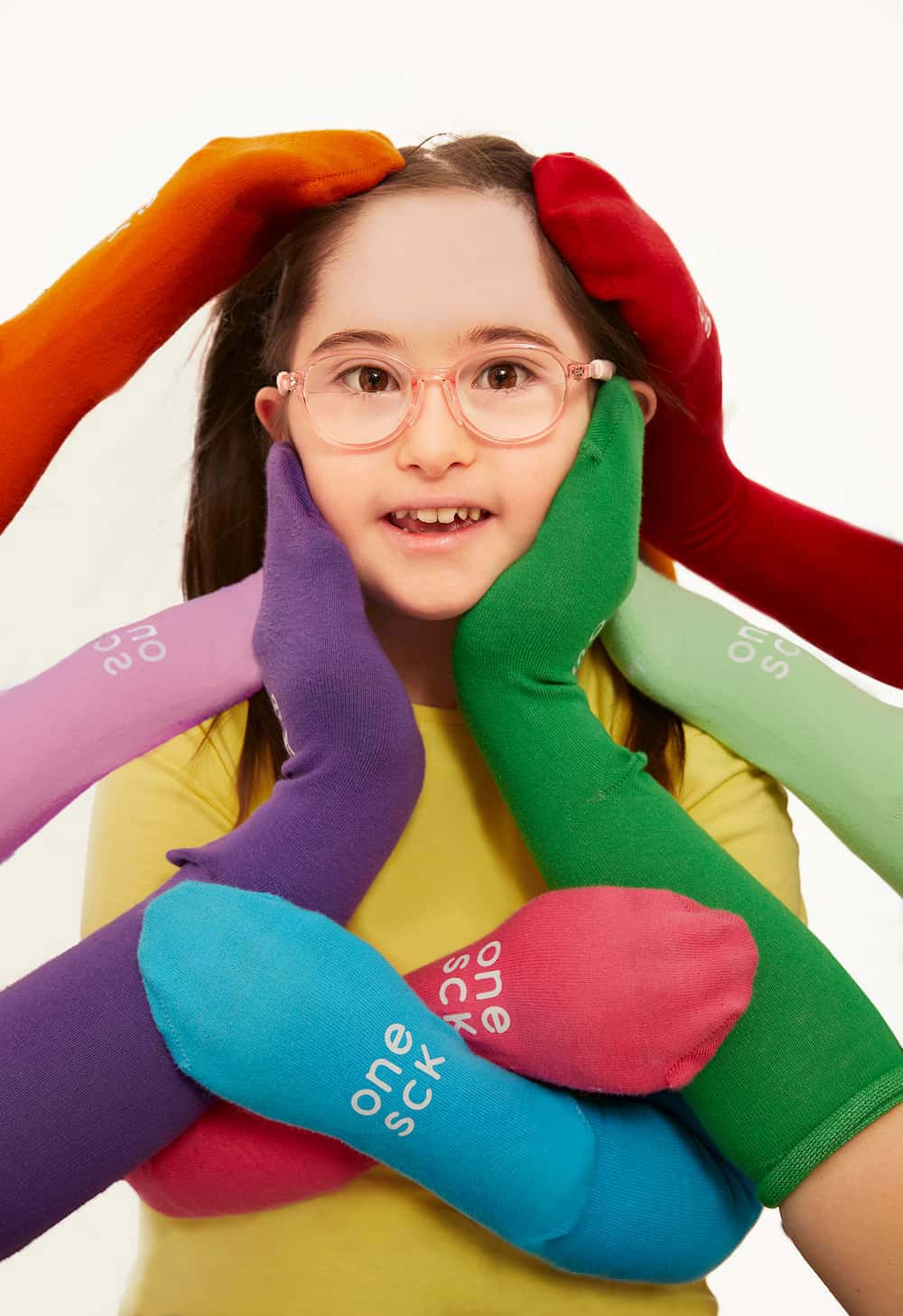 A young girl with glasses is surrounded by multiple colorful, soft fabric arms reaching toward her face, each printed with the brand name 'oneuck'. The background is a clean white studio backdrop.